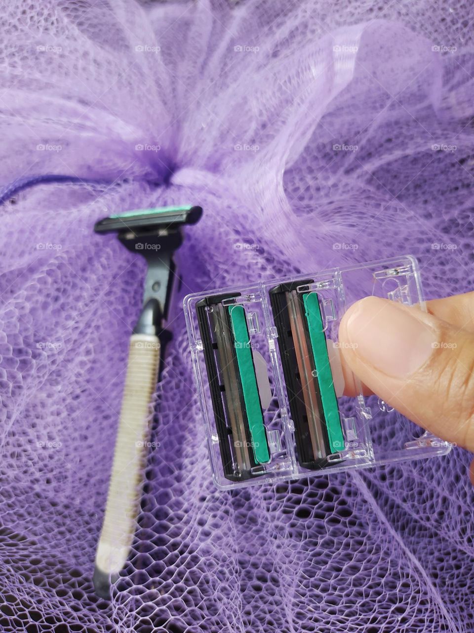 Gray razor, blade refill, purple netting background