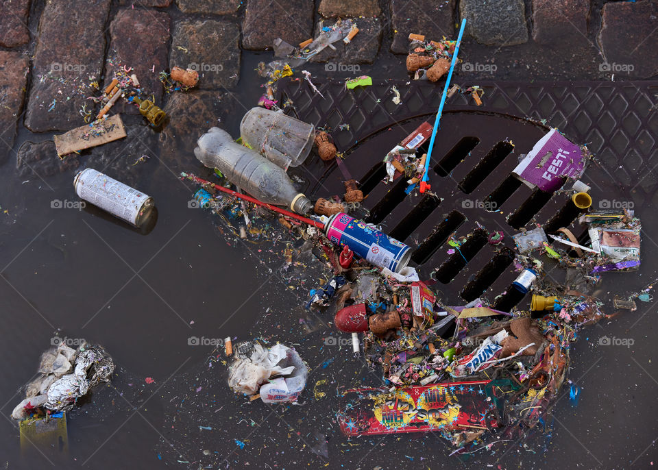 Helsinki, Finland - May 1, 2017: Plastic and other trash over sewer and partly floating in a puddle on cobble street after first of May celebrations. 