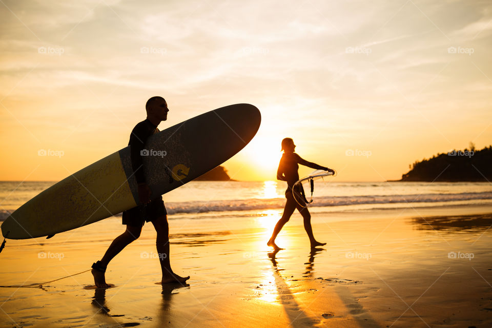 Silhouettes of two surfers on sunset 