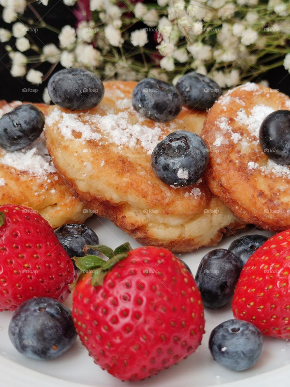 cheese pancake sprinkled with white powder. Berries of black blueberries and red strawberries lie on cheese pancake