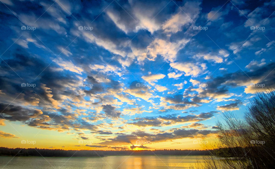 Colorful and dramatic sunset sky with fluffy clouds over a rural forest lake