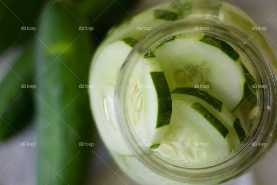 Overhead view of cucumber-infused water in a half-gallon mason jar with cucumbers on a white dish towel