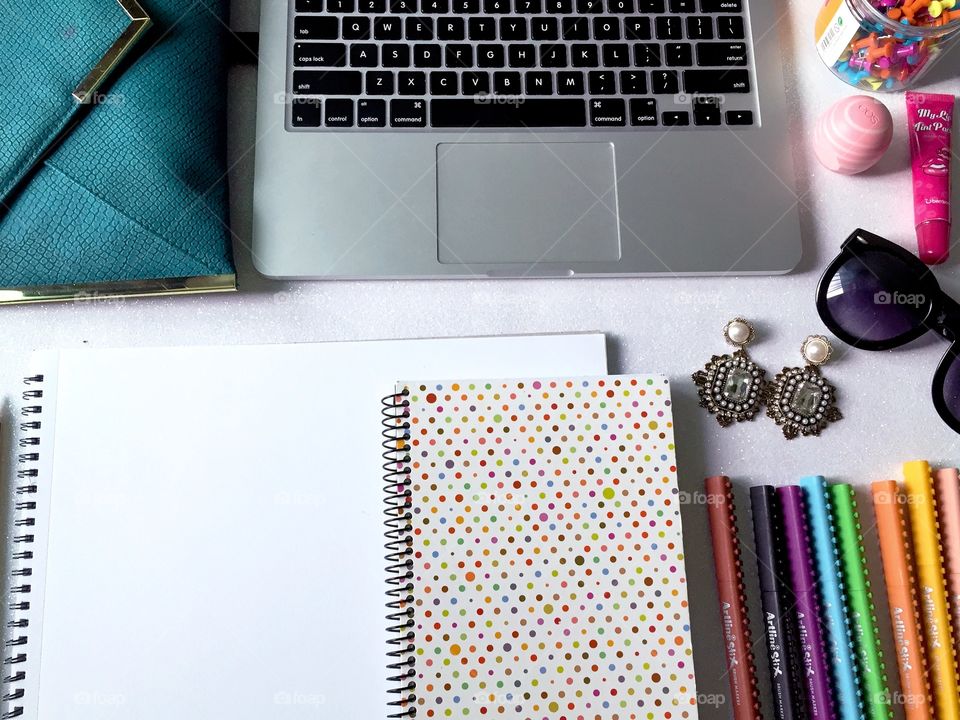 Top view of women's work desk with stationary, laptop, notebook, fashion accessories and empty sketch book.