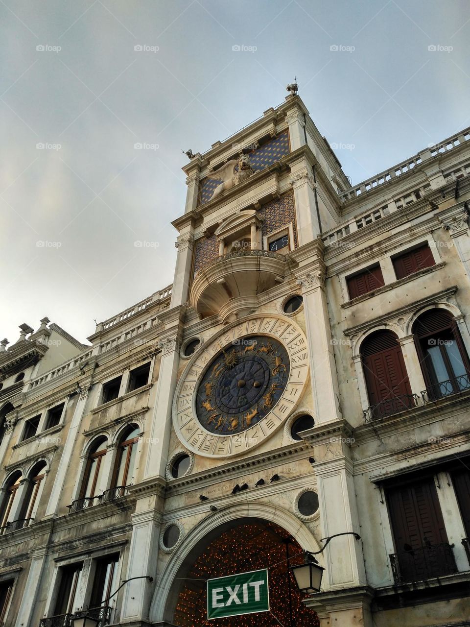 Photo from below a building. It has a clock with errors in its Roman numerals. Various geometric shapes in its structure and textures.
