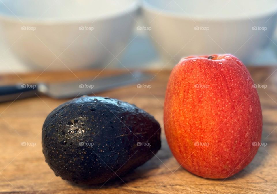 An avocado and an apple on a cutting board