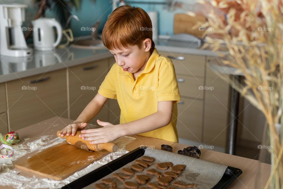 Child red-haired boy bakes cookies at home in the kitchen, dressed in a yellow T-shirt. Craft product, do it yourself