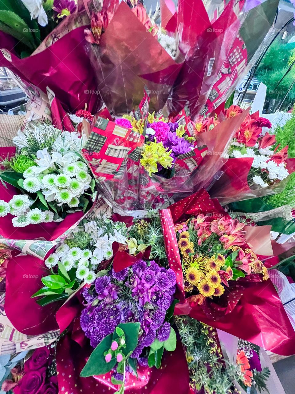Uma exibição vívida de buquês florais variados embrulhados em papéis vibrantes, exibindo uma mistura de cores, incluindo vermelho, roxo, amarelo e branco, com folhagens verdes exuberantes, criando uma atmosfera alegre e animada.
