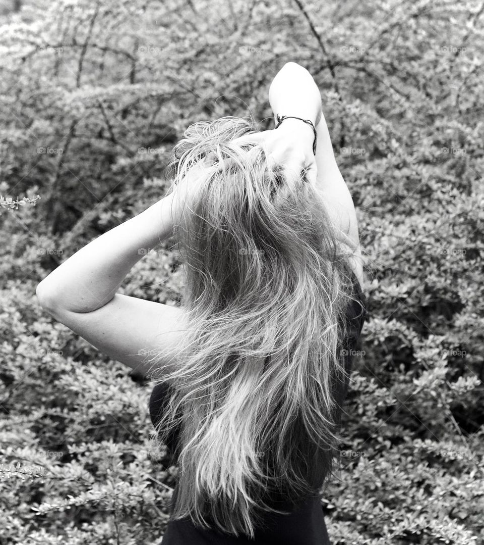 Woman tossing her hair while pulling a ponytail among shrubs in full bloom