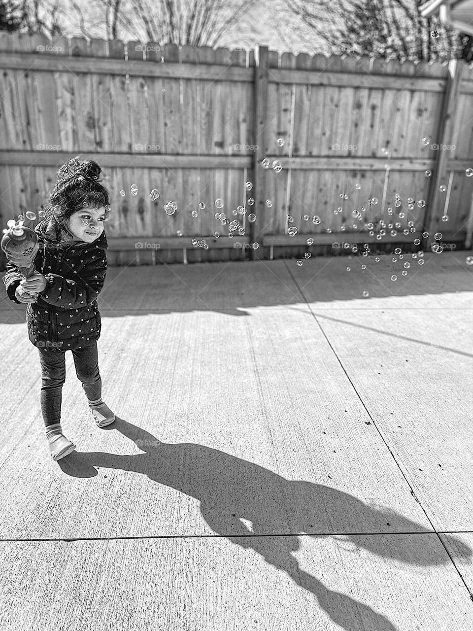 Toddler girl blowing bubbles outside, a trail of bubbles follow toddler girl, swinging a bubble maker to make lots of bubbles, black and white portrait of bubbles and toddler, monochrome portraits, circles in every day life, circular shapes 