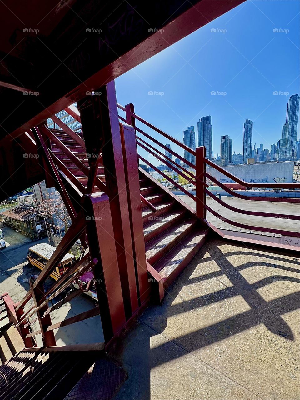 This is the middle platform of the red metal staircase of the “Pulaski Bridge” at “Newtown Creek” in LIC, Queens. The afternoon sun casts dramatic shadows that combine with the structure thus creating interesting patterns. 2024. Hypnotic Productions