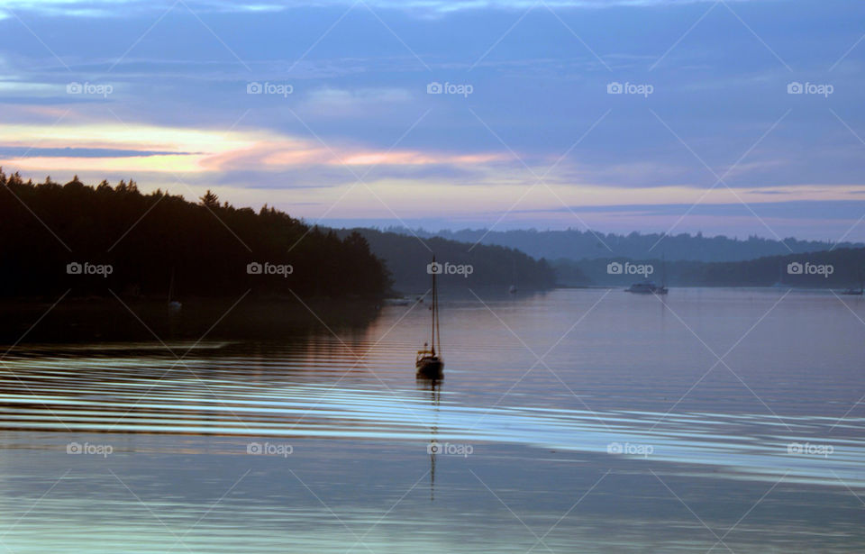 Sailboat sits on the serene day as the sun sets