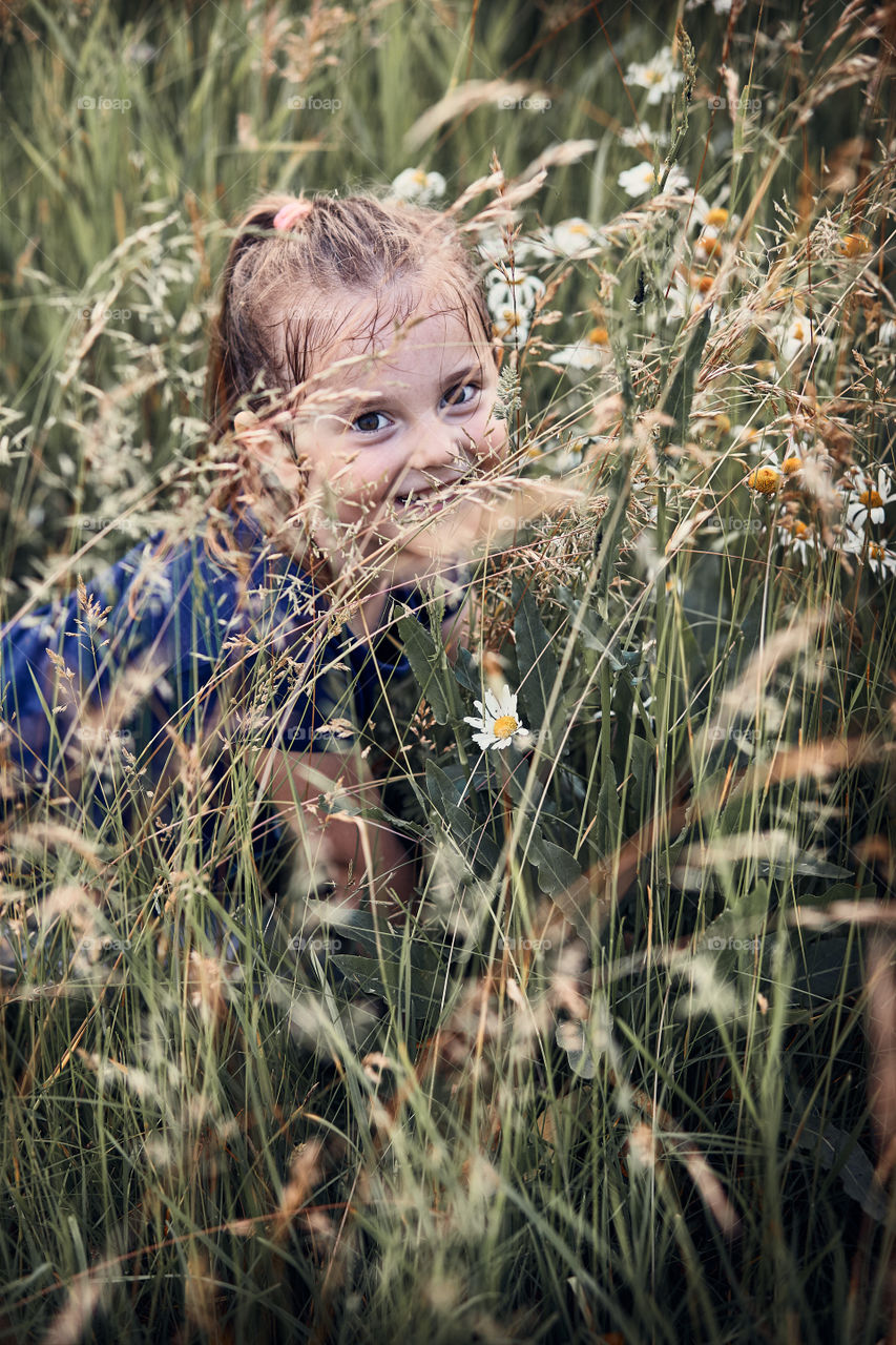 Little happy kid playing in a tall grass in the countryside. Candid people, real moments, authentic situations