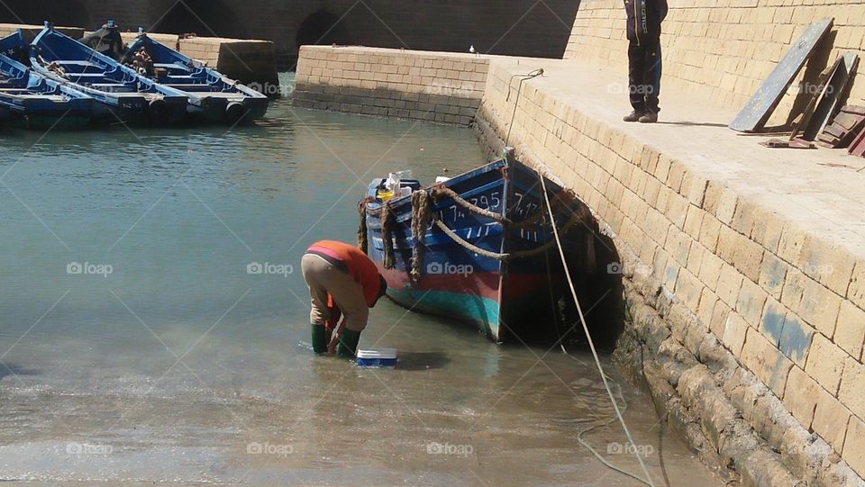  A sailor cleans his boat by the dock.