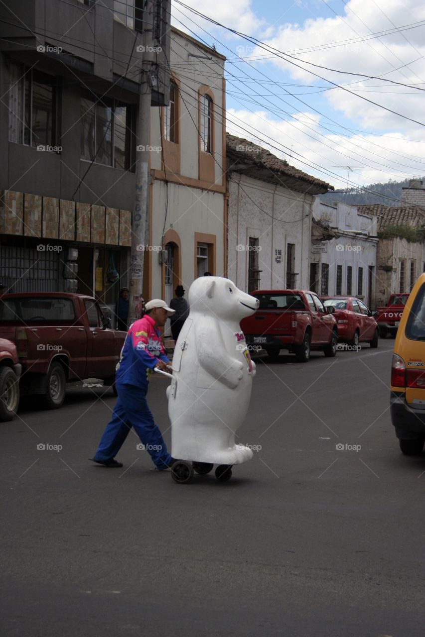 Man walking a huge polar be a r with coca cola inside it.  He's a vendor in Riobamba Ecuador.