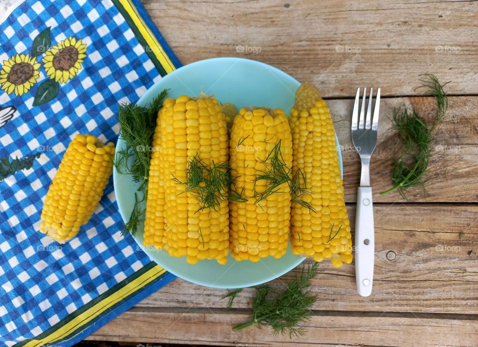 sweet boiled corn in a blue plate on a table in the garden.