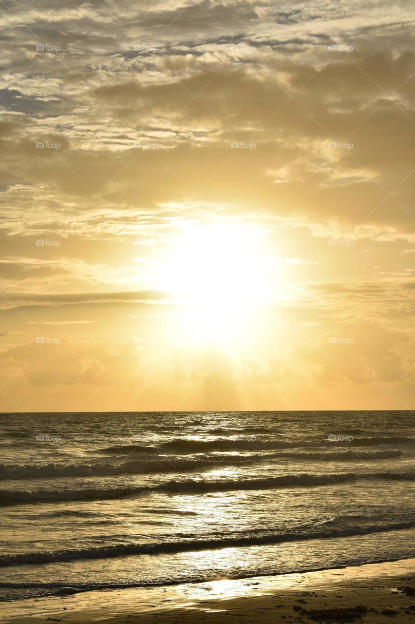 Stunning sunset over Daytona Beach in Florida. Yellow sunlight illuminating the sky and reflecting on the ocean waves.