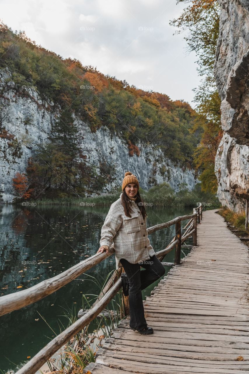 Portrait of happy girl standing on wooden footpath by lake in autumn