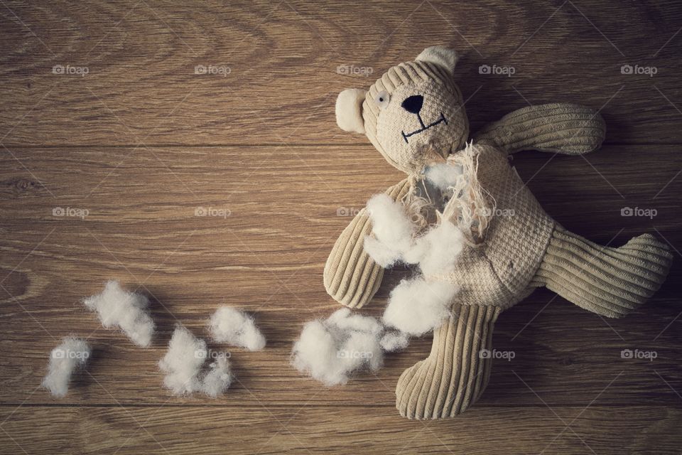 A sad and abandoned teddy bear with his stuffing pulled out on a wooden floor.