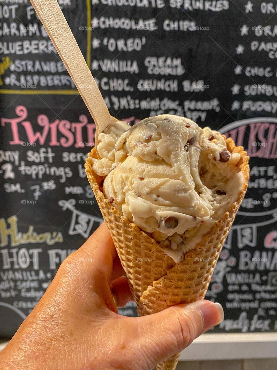 Summer treats - ice cream in a waffle cone is always a good treat.  Hand in frame holding cone with spoon in ice cream.