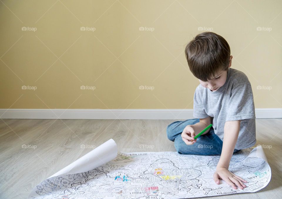 pensive boy examines a large coloring book on the floor