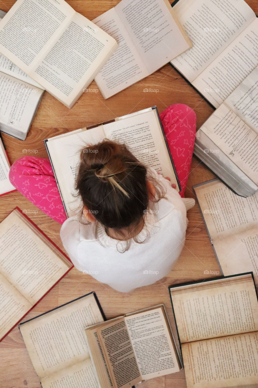 A child reading a book, surrounded by books