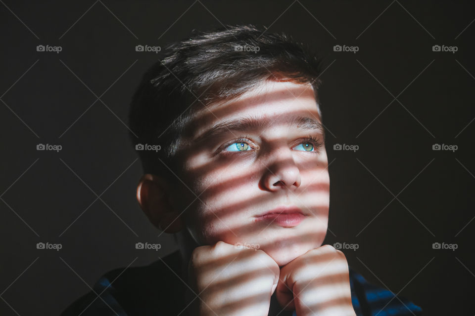 Close-up of thoughtful boy looking away against wall with sunlight falling on his face. 