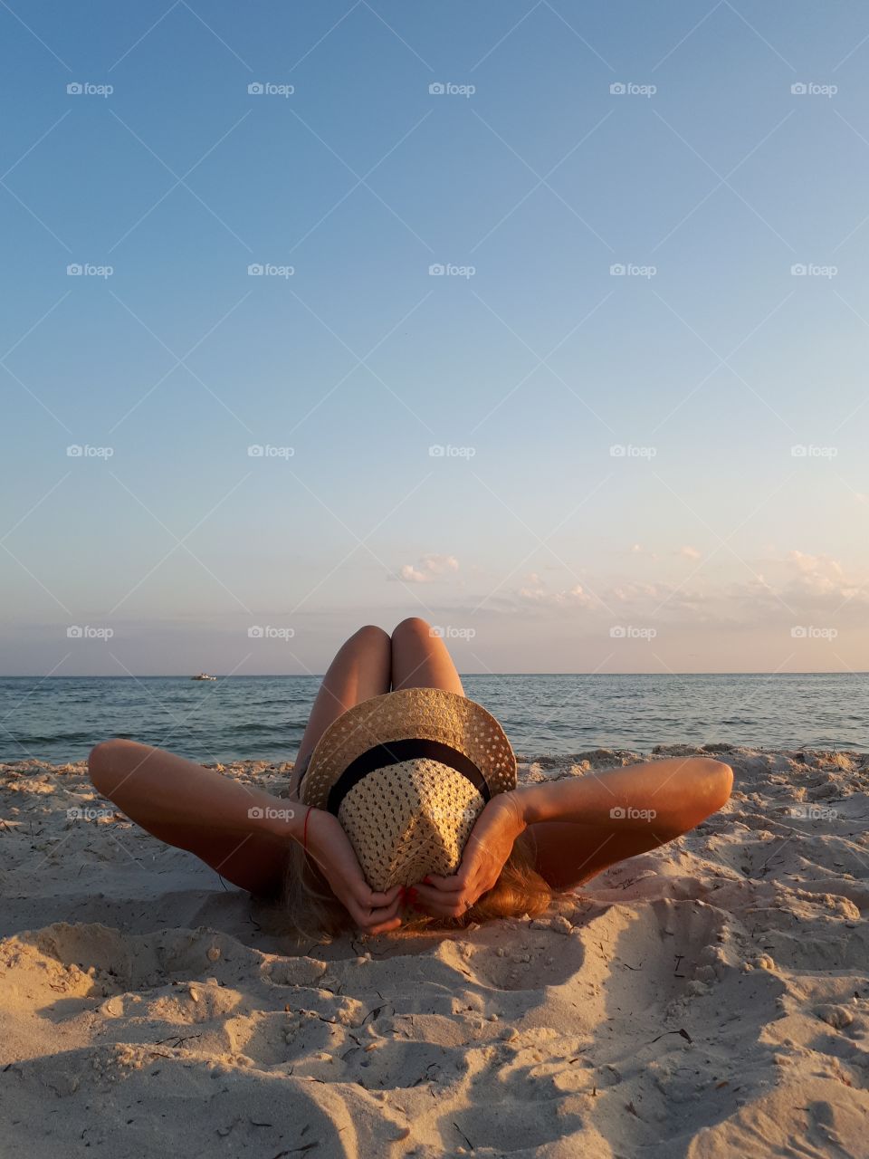 Woman lying down at the sand beach at straw hat