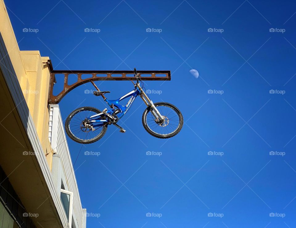 Bicycle hanging against a blue sky with a half moon