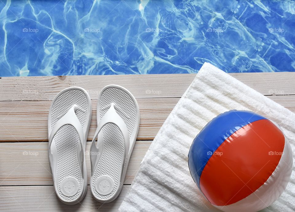 Flip flops beside a towel and a beach ball with a wide blue and white stripe