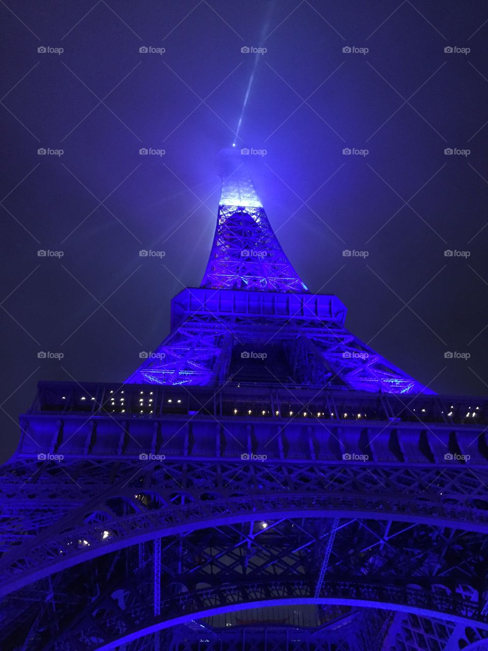 Beneath the Eiffel Tower lit up in blue.