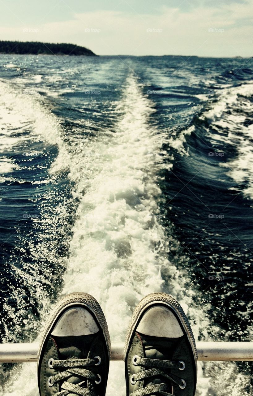 Person's canvas shoes against water wake