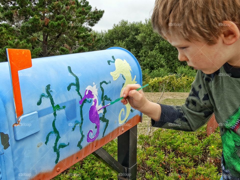 Boy Painting A Picture. Young Boy Painting Seahorses On A Mailbox
