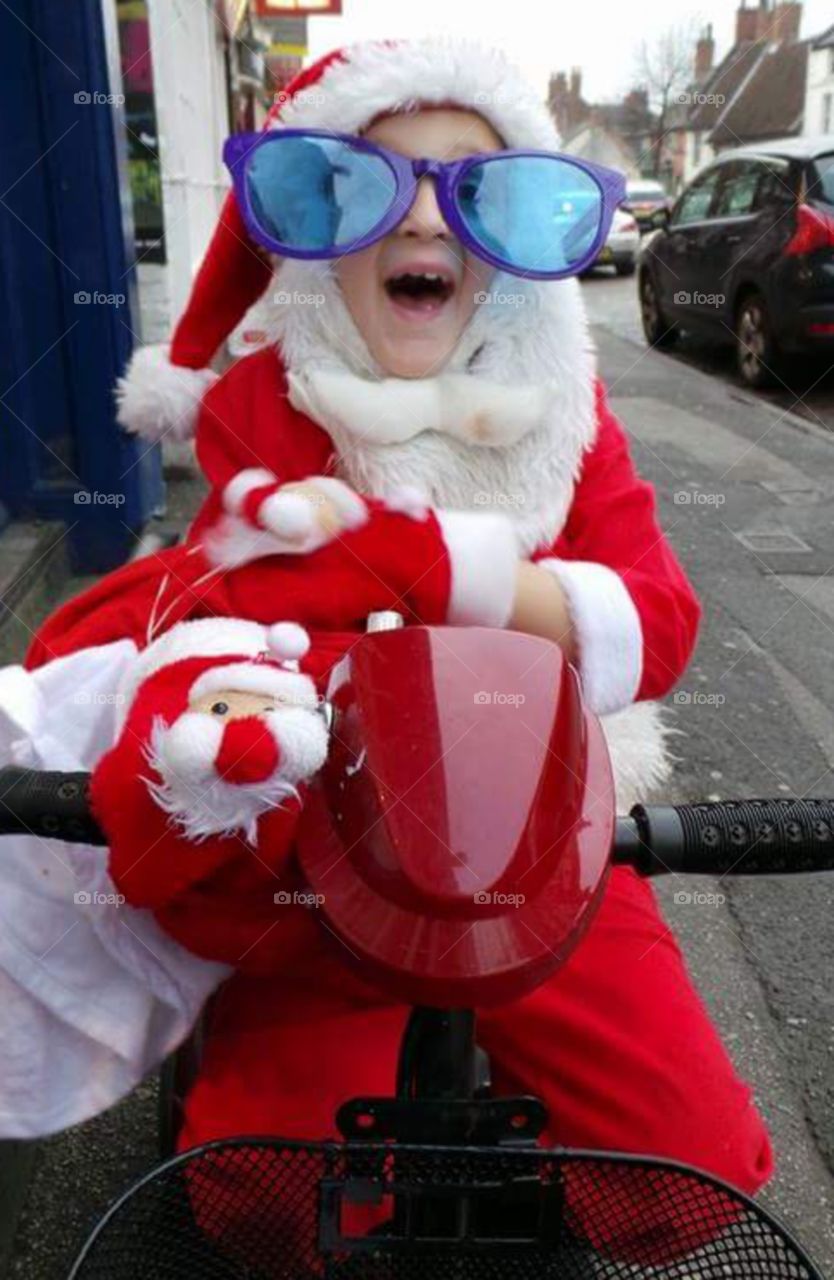 obscure child dressed as santa with jumbo comical sunglasses on a mobility scooter