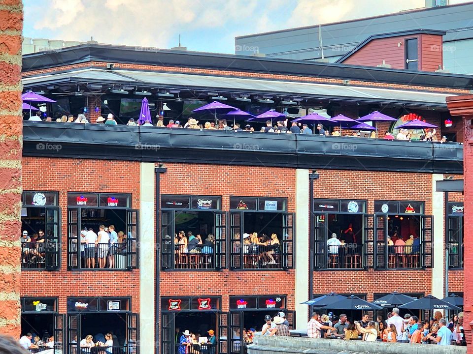 A large crowd congregates on multiple floors of different restaurants during a summer celebration