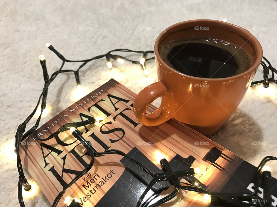 Book with an orange cup of coffee and Christmas yellow lights.