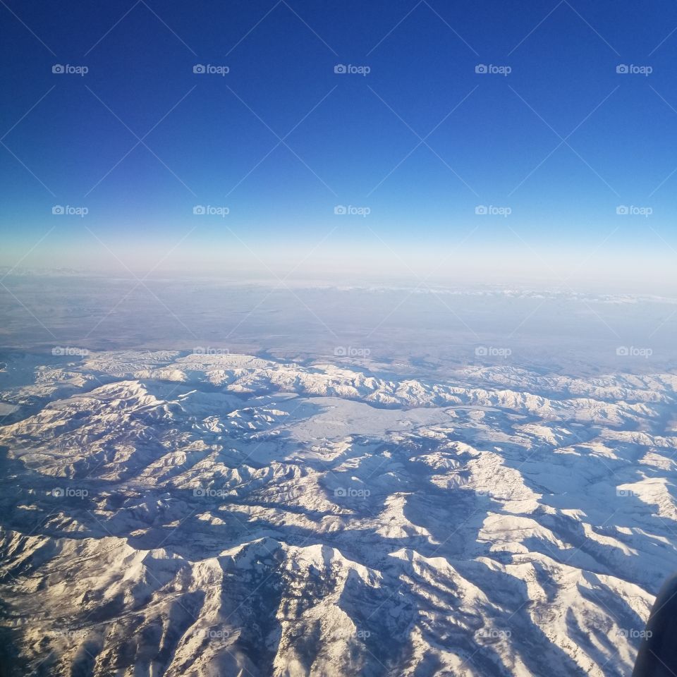 airplane view of snow covered mountains with a blue sky