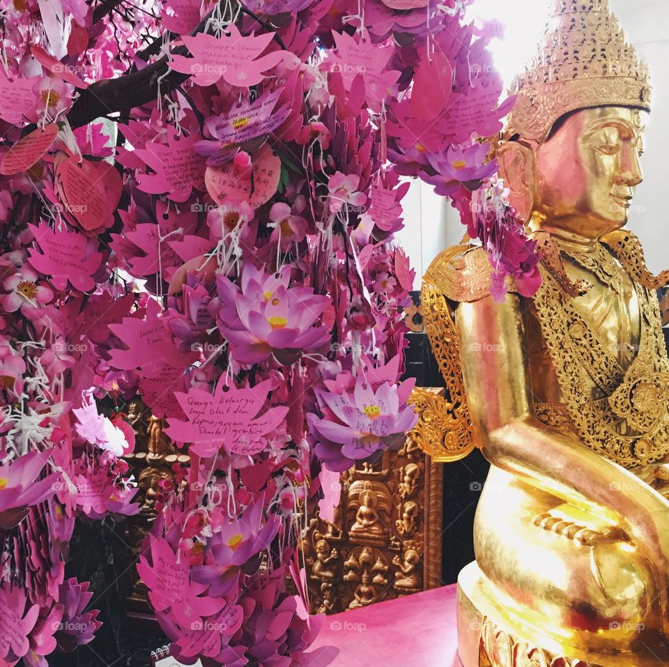 Pink paper leaves with well wishes written on them hang beside a golden Buddha statue in Medan, Indonesia.