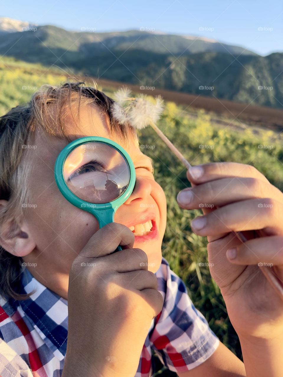 Boy looking at a dandelion through a magnifying glass