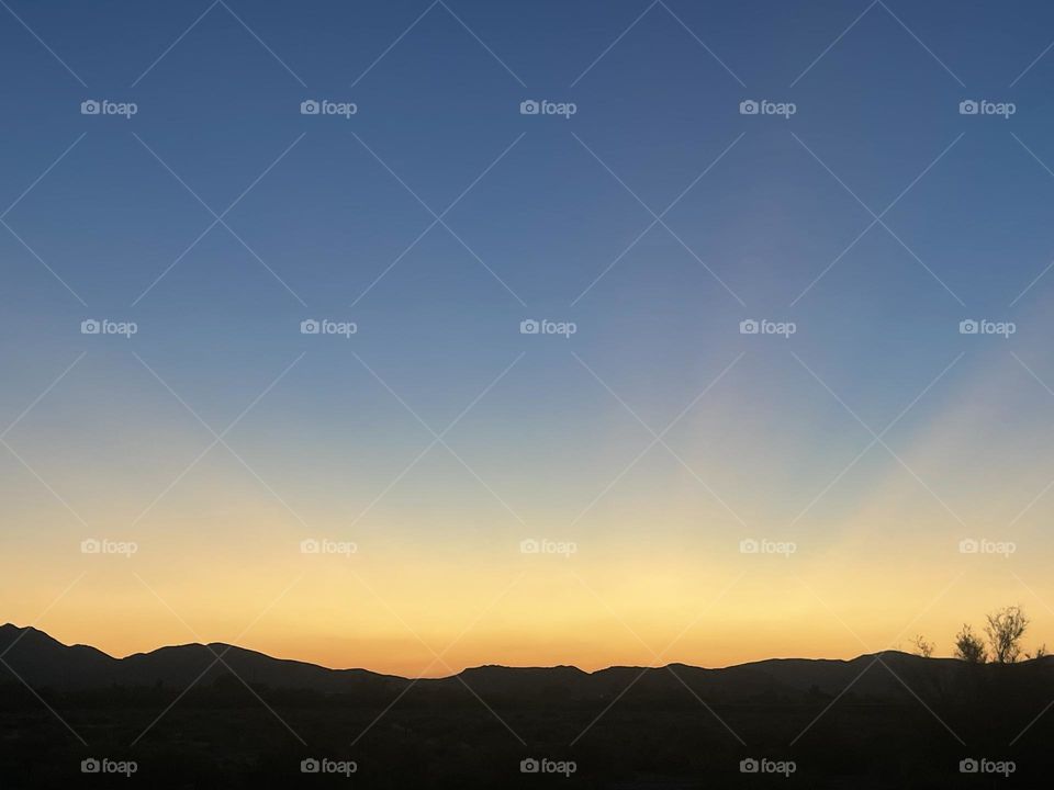 A blue and yellow sunset with mountains below.