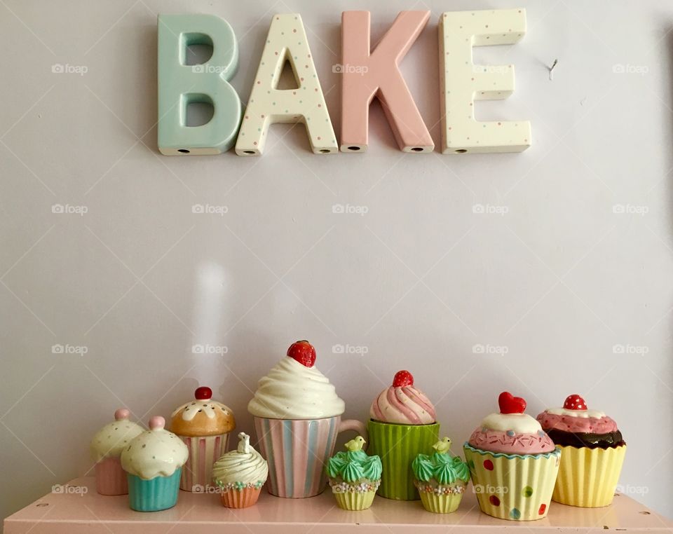 Ceramic Bake letters on a wall painted marshmallow colour with cupcake trinket boxes and containers in the kitchen 
