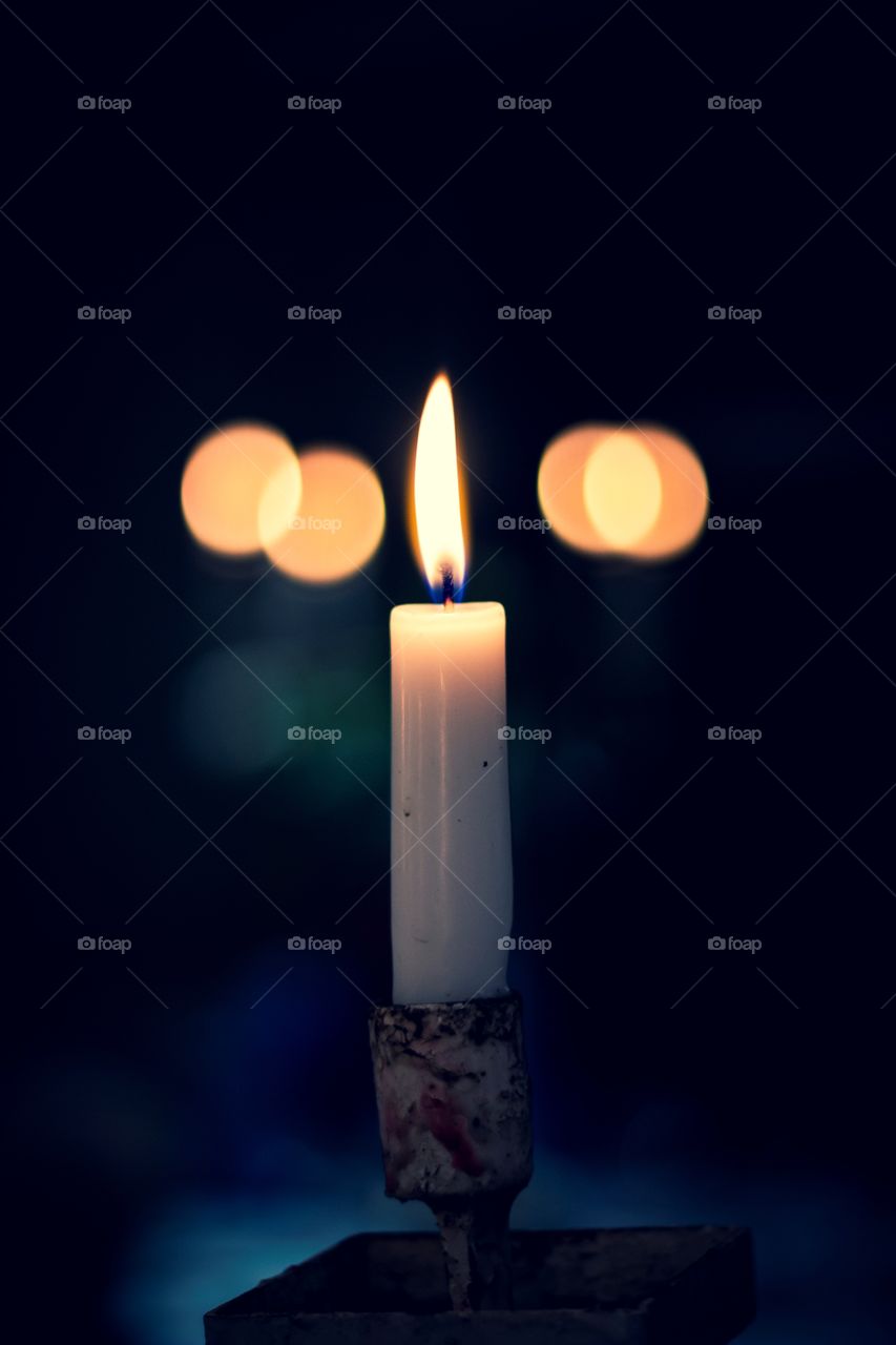 A portrait of a lit candle in a moody relaxing scene. the bokeh balls in the back are other burning candles.