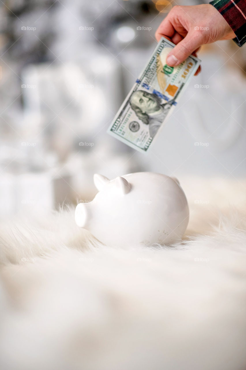 piggy bank with 100 dollars banknote in festive New Year atmosphere of scenery.  Magical bokeh with Christmas tree and bright lights.