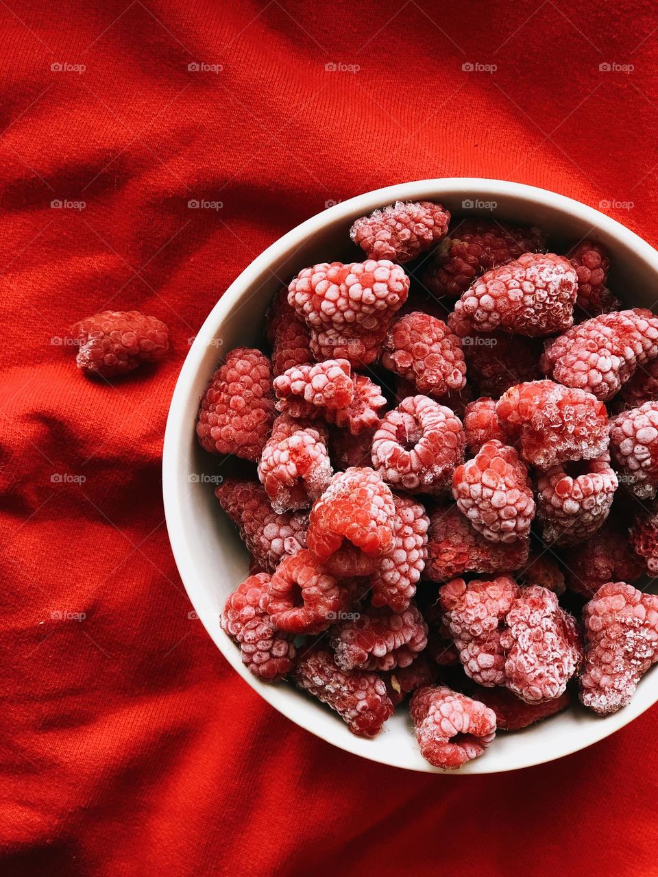 A plate of frozen raspberries on a red background, nobody 