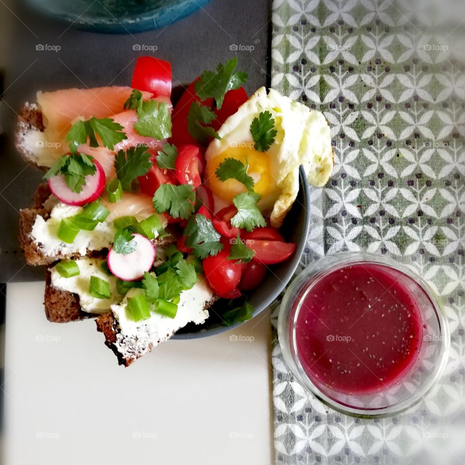 Bowl with salmon and cream cheese sandwich, salad and a fried egg next to a berry smoothie