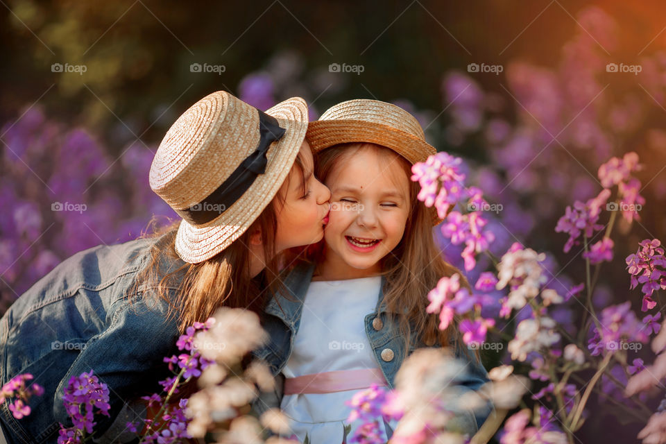 Little sisters in a blossom meadow at sunset 