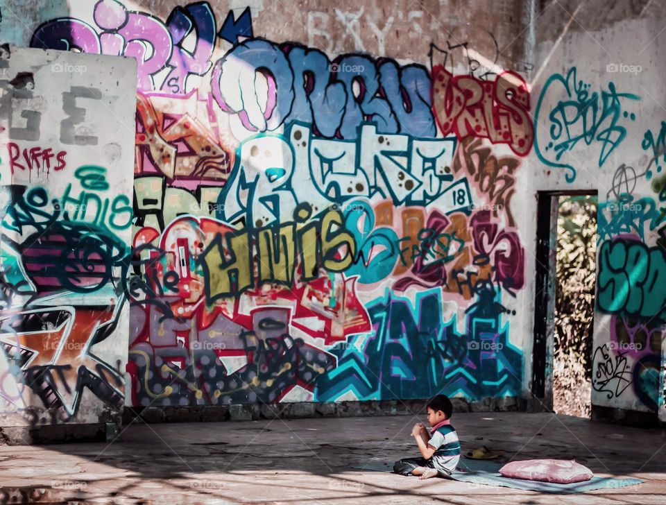a little boy sitting in an empty room like a house full of graffiti