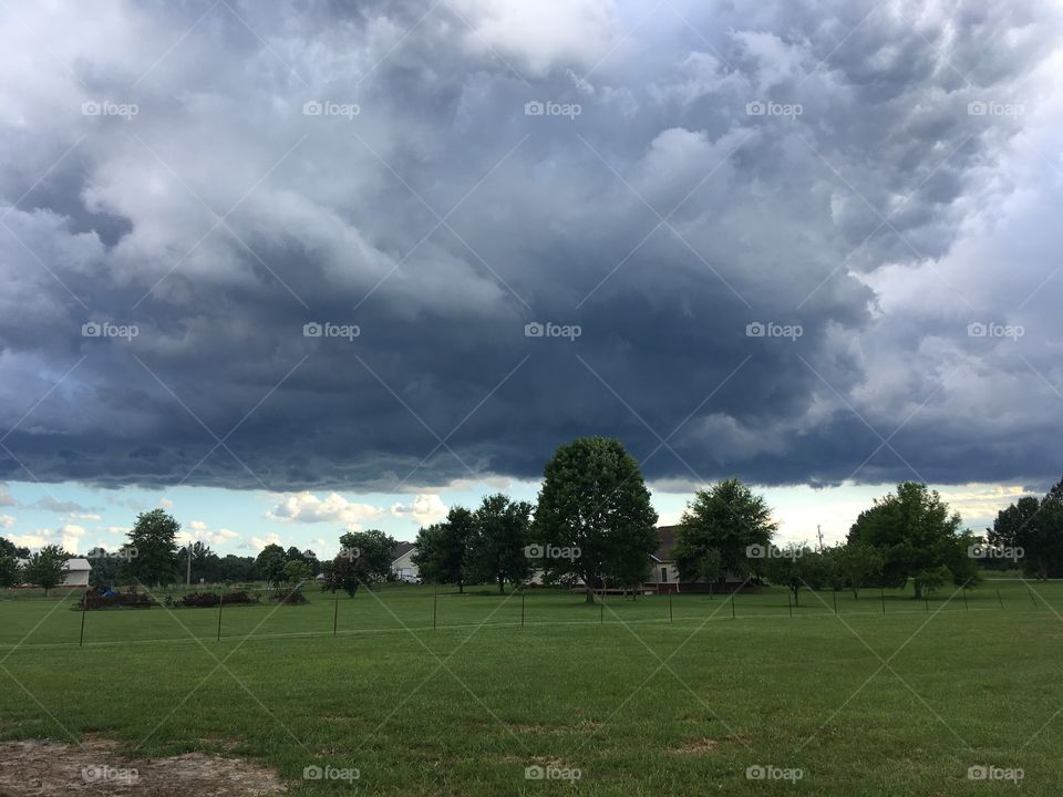 Interesting and different contrast of grass trees sky and dark puffy clouds from the porch.