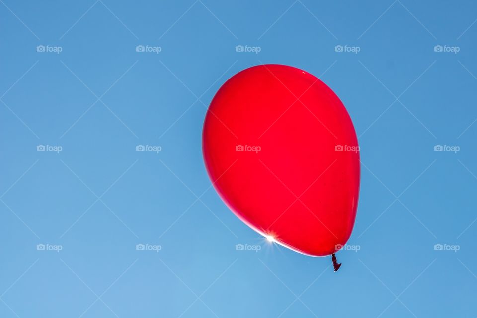 Horizontal photo of a bright red balloon against a blue sky and the sun gleaming off the edge of the balloon