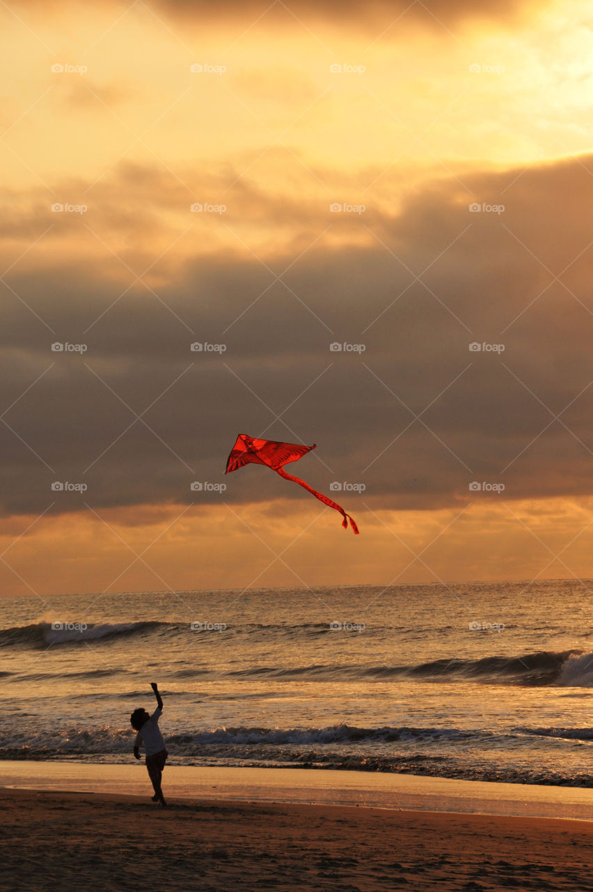 A boy flying a kite on the beach at sunset 