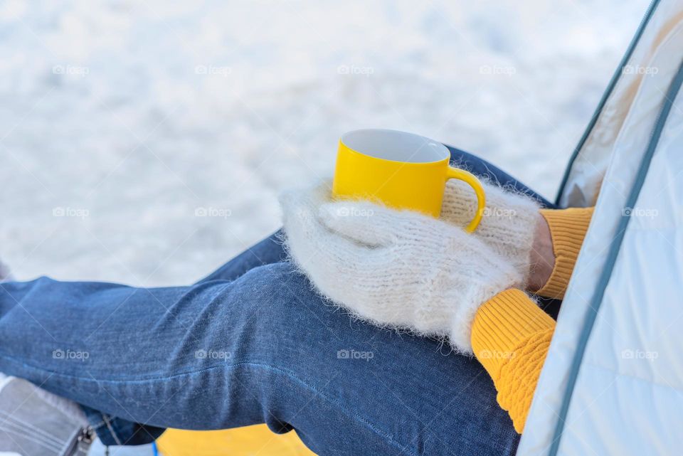 Bright yellow cup in girl hands with white mittens against white snow background. Winter outdoor activity, lifestyle concept. Time to break. Slow life. Winter scene with copy space.